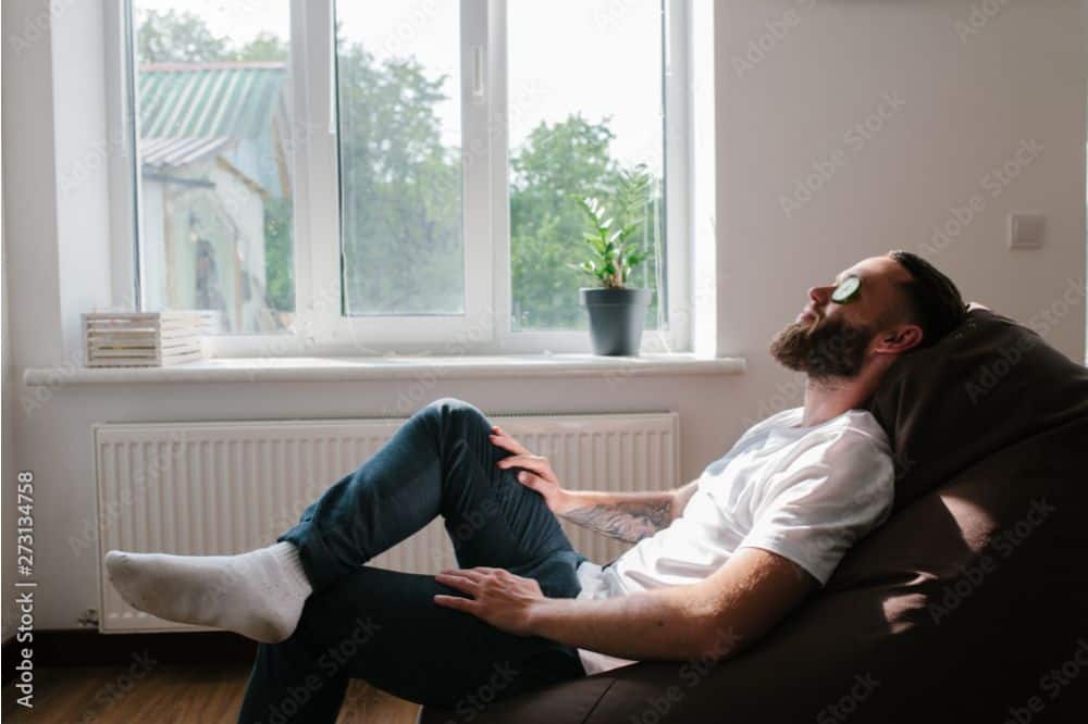 young man relaxing with cucumber on his eyes sitting in big comfortable chair