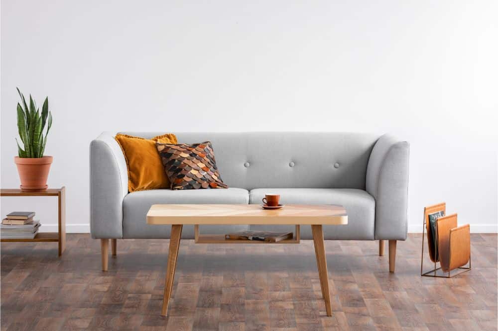 Wooden coffee table in the middle of elegant living room with grey couch and magazine rack