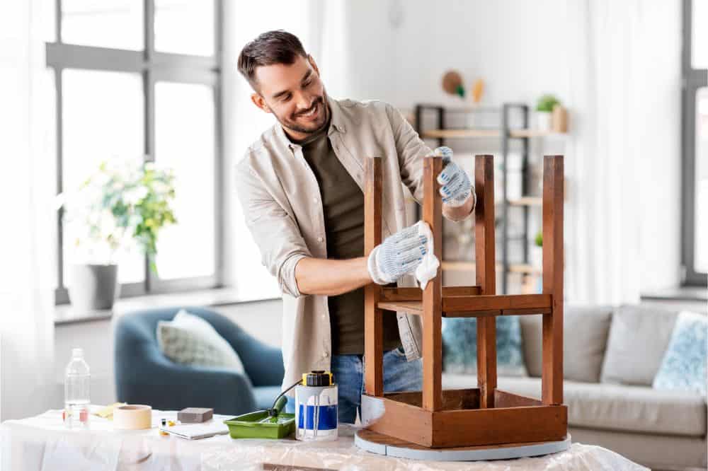 happy smiling man degreasing old wooden table or chair surface with tissue